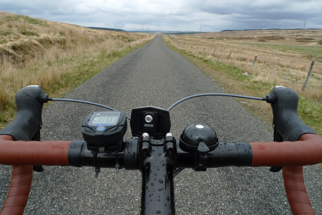 A view from a bicycle showing the handlebars and an empty road near Forsinard, Sutherland