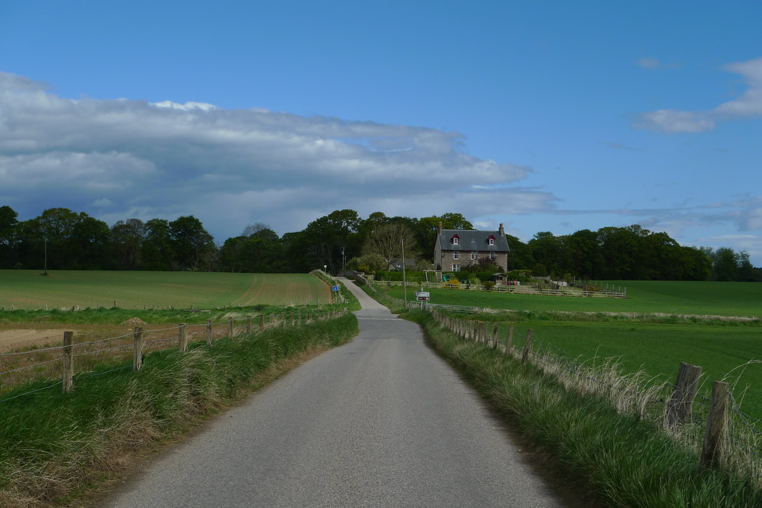 A road heading to Brodie Castle, with fields and a large farm house
