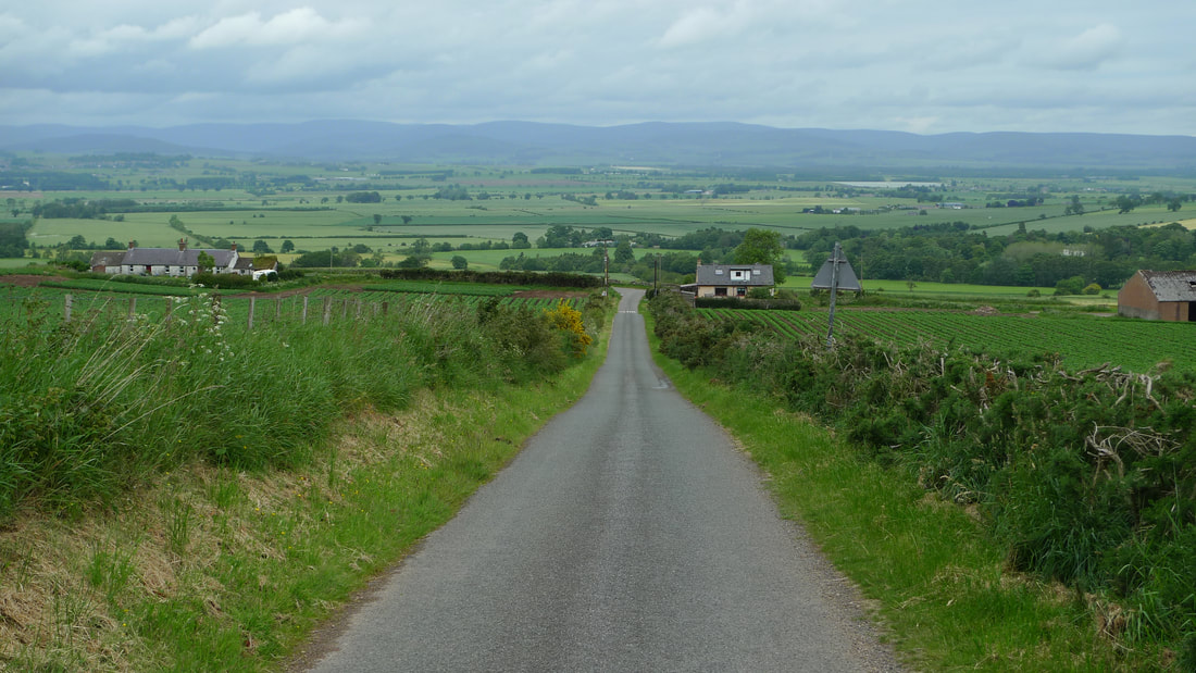 A road on the cycling route to Glamis Castle with a downhill section and views across fields to the Cairngorms