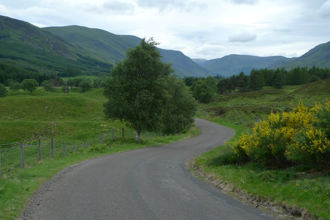 A road twists through Glen Clova with mountains ahead and trees all around