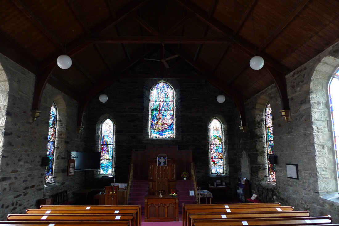Inside Kilbrandon Church. There are bare stone walls and stained glass windows.
