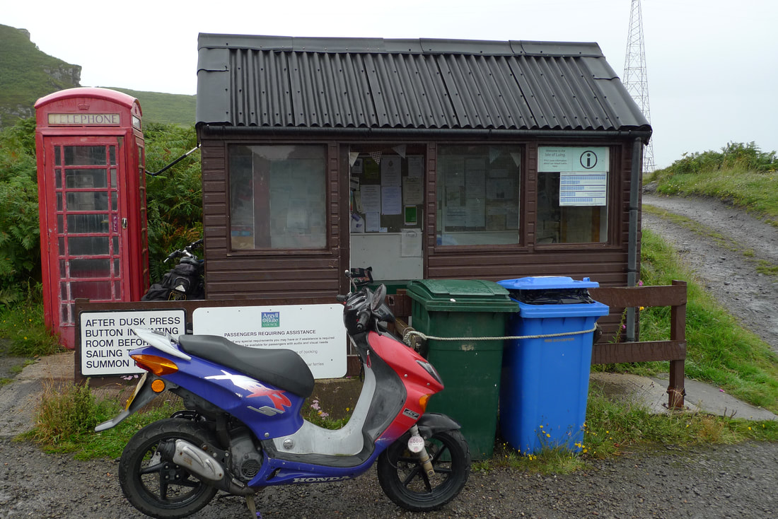 Isle of Luing ferry waiting room. A moped is parked in front and there's a red telephone box.