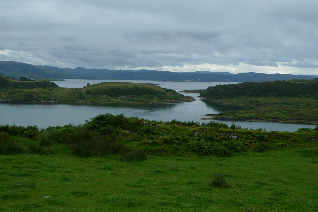 The view from the Isle of Luing. In the foreground is the sea and there's a horizon of hills