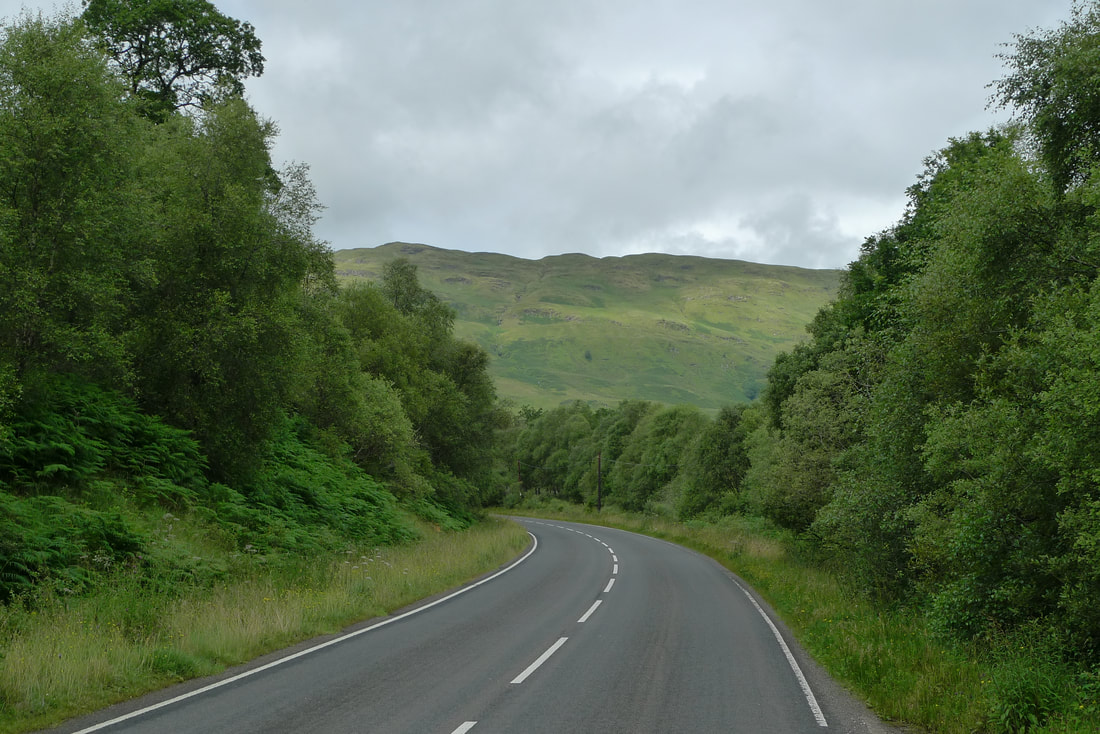 Trees on each side of the A819 road, with a hillside on the horizon